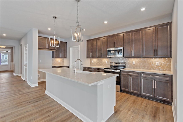 kitchen with a kitchen island with sink, stainless steel appliances, light stone countertops, sink, and decorative light fixtures