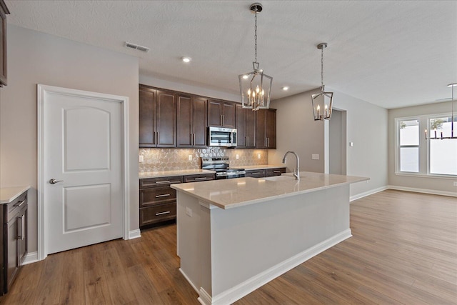 kitchen with sink, tasteful backsplash, dark brown cabinetry, a kitchen island with sink, and appliances with stainless steel finishes