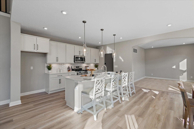 kitchen with white cabinets, an island with sink, decorative light fixtures, and appliances with stainless steel finishes