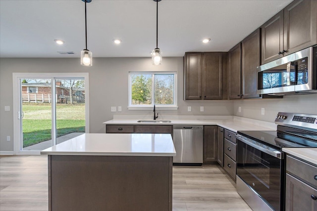 kitchen featuring appliances with stainless steel finishes, dark brown cabinetry, sink, a center island, and hanging light fixtures