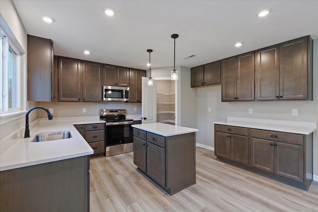 kitchen featuring pendant lighting, a center island, sink, light wood-type flooring, and stainless steel appliances