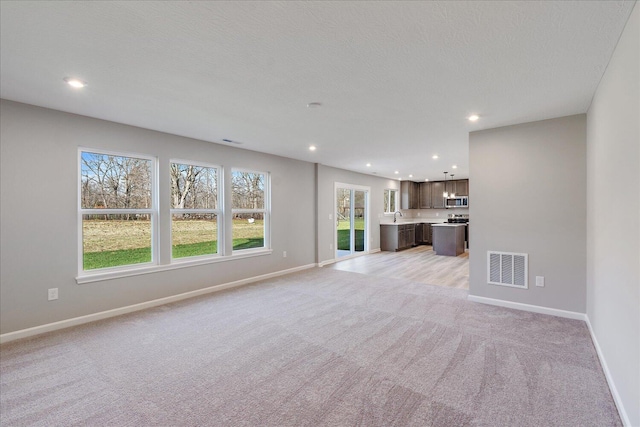 unfurnished living room featuring sink and light carpet