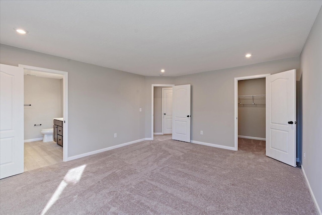 unfurnished bedroom featuring light colored carpet, a walk in closet, connected bathroom, and a closet