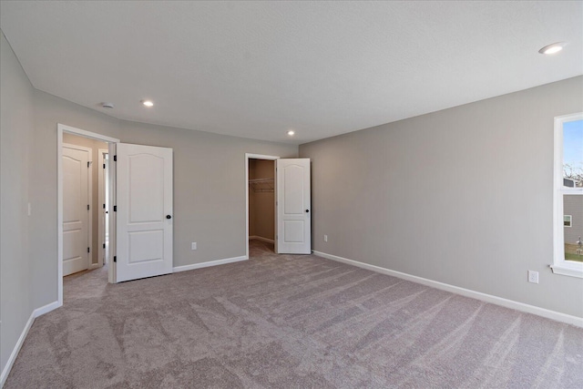 unfurnished bedroom with a walk in closet, light colored carpet, and a closet