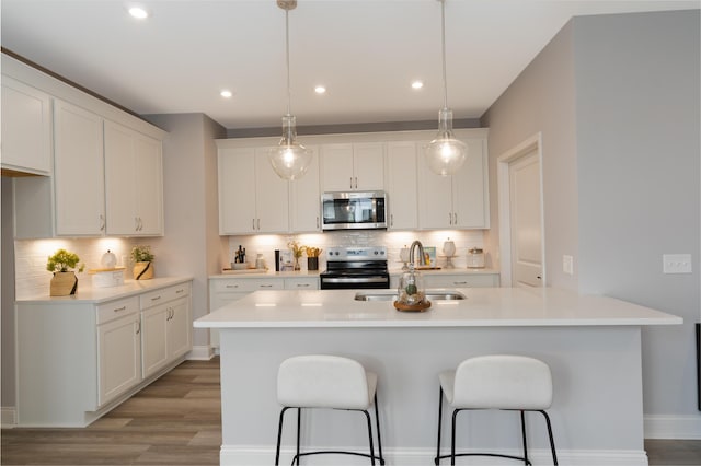 kitchen with white cabinets, light wood finished floors, appliances with stainless steel finishes, a sink, and a kitchen breakfast bar