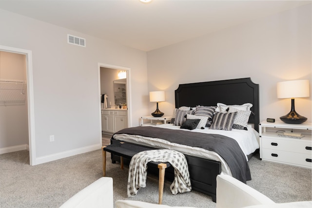 bedroom featuring connected bathroom, carpet flooring, a walk in closet, baseboards, and visible vents