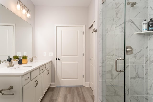 bathroom featuring double vanity, a sink, a stall shower, and wood finished floors