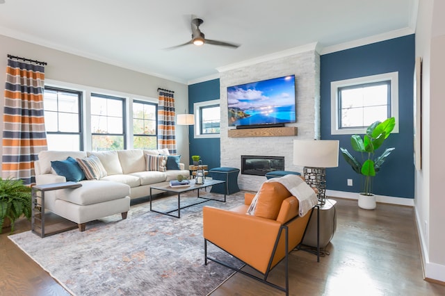 living room with a wealth of natural light, a stone fireplace, crown molding, and hardwood / wood-style flooring