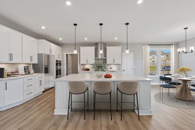 kitchen featuring decorative light fixtures, stainless steel appliances, wall chimney exhaust hood, and a large island