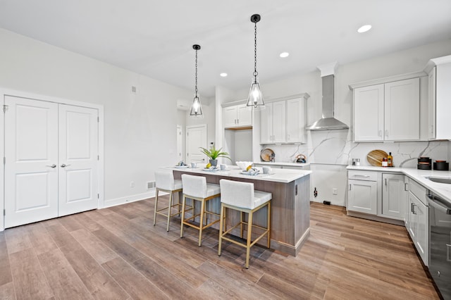 kitchen featuring pendant lighting, a kitchen breakfast bar, wall chimney exhaust hood, a kitchen island, and white cabinetry