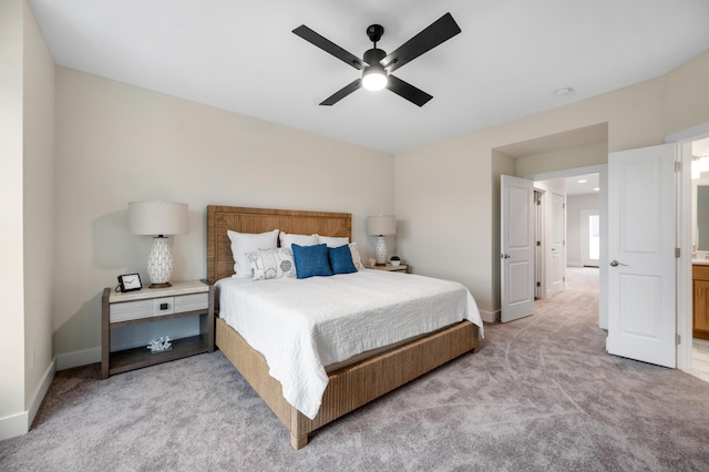 bedroom with ceiling fan, light colored carpet, and ensuite bath
