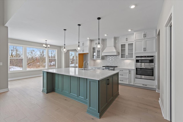 kitchen with white cabinets, a center island with sink, custom range hood, and decorative backsplash