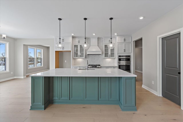 kitchen with a center island with sink, decorative light fixtures, white cabinetry, and premium range hood