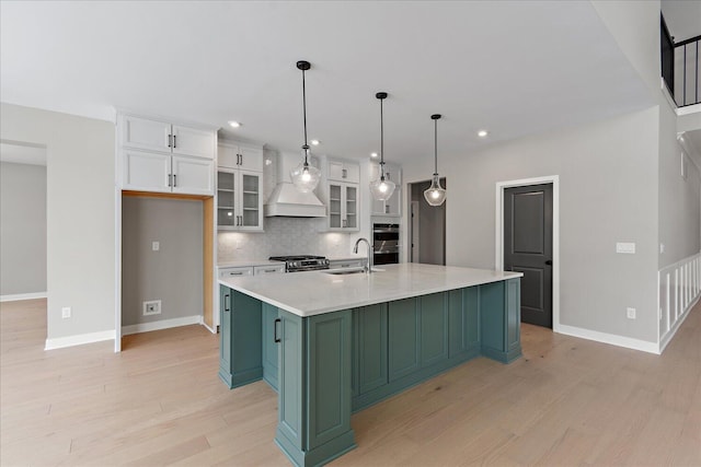 kitchen featuring custom exhaust hood, a kitchen island with sink, backsplash, white cabinetry, and appliances with stainless steel finishes