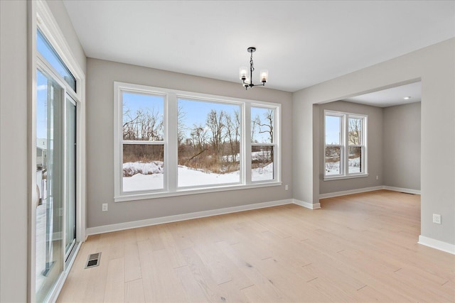 unfurnished dining area featuring a healthy amount of sunlight, light hardwood / wood-style floors, and an inviting chandelier