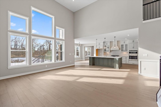 unfurnished living room with a notable chandelier, light hardwood / wood-style floors, a towering ceiling, and sink