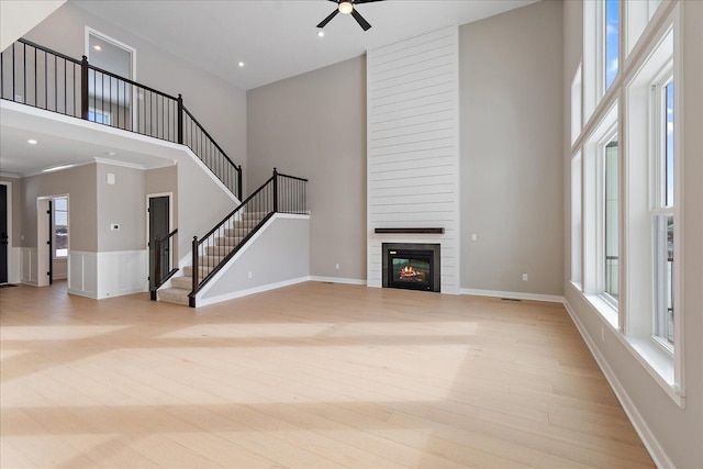 unfurnished living room featuring a towering ceiling, a tiled fireplace, ceiling fan, and light hardwood / wood-style floors