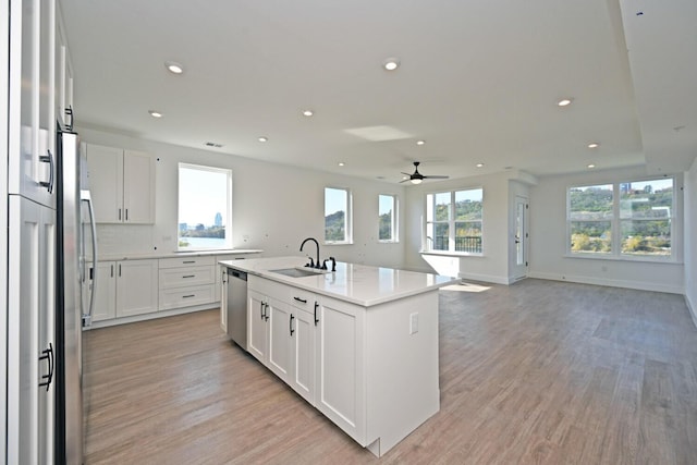 kitchen with appliances with stainless steel finishes, sink, white cabinets, a center island with sink, and light hardwood / wood-style flooring