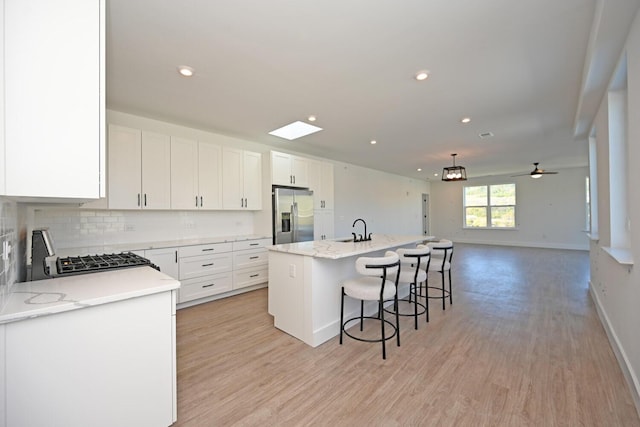 kitchen featuring a breakfast bar, white cabinetry, stainless steel fridge with ice dispenser, a kitchen island with sink, and stove