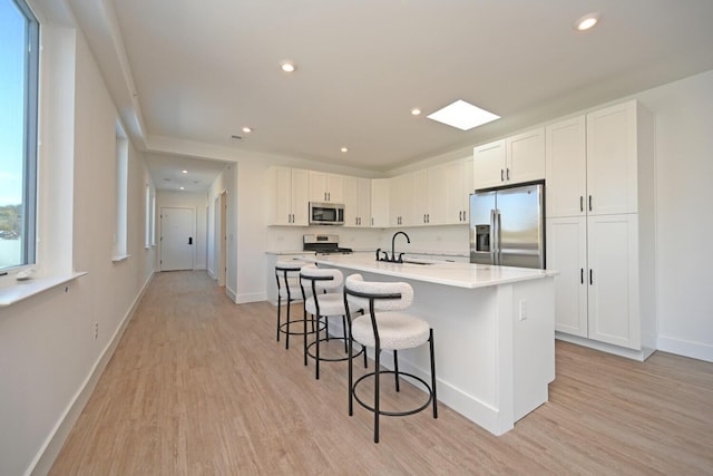 kitchen featuring sink, appliances with stainless steel finishes, white cabinetry, light hardwood / wood-style floors, and a center island with sink