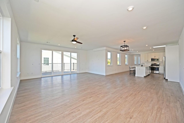 unfurnished living room featuring sink, ceiling fan with notable chandelier, and light wood-type flooring