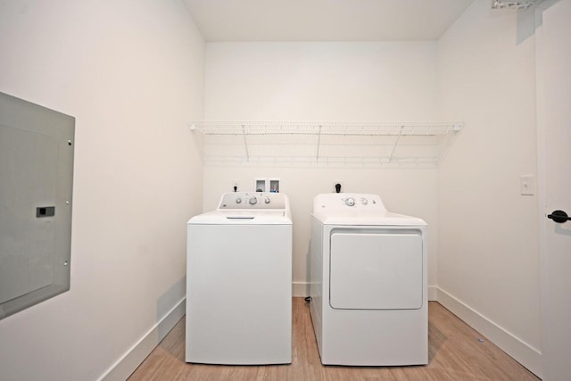 laundry area with light hardwood / wood-style flooring, washing machine and dryer, and electric panel