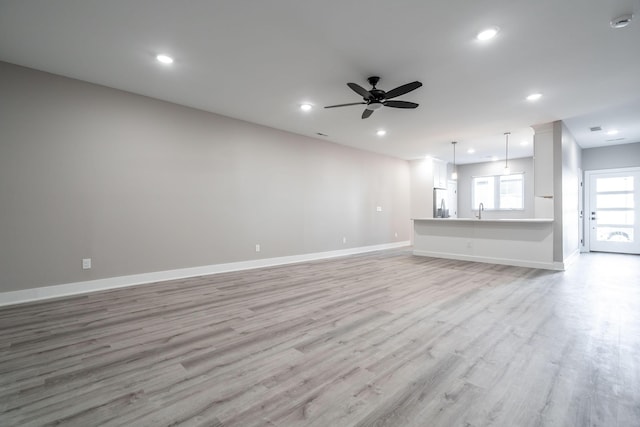 unfurnished living room with ceiling fan, light wood-type flooring, and sink