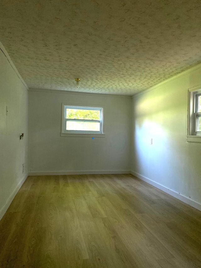 empty room featuring light wood-type flooring, a textured ceiling, and ornamental molding