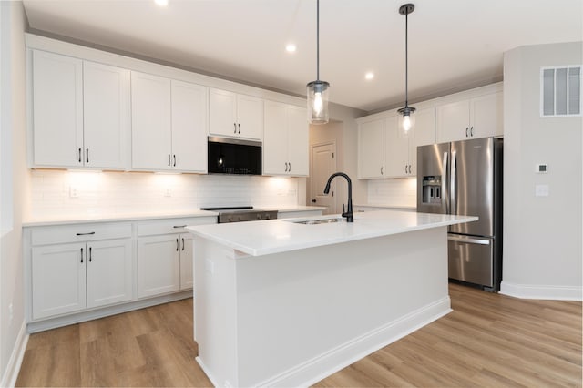 kitchen featuring pendant lighting, sink, stainless steel fridge, white cabinetry, and a center island with sink