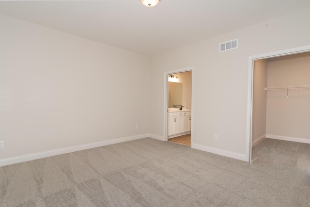 unfurnished bedroom featuring connected bathroom, a spacious closet, light carpet, and a closet