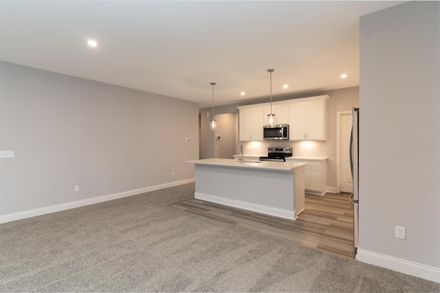 kitchen featuring appliances with stainless steel finishes, an island with sink, sink, white cabinets, and hanging light fixtures