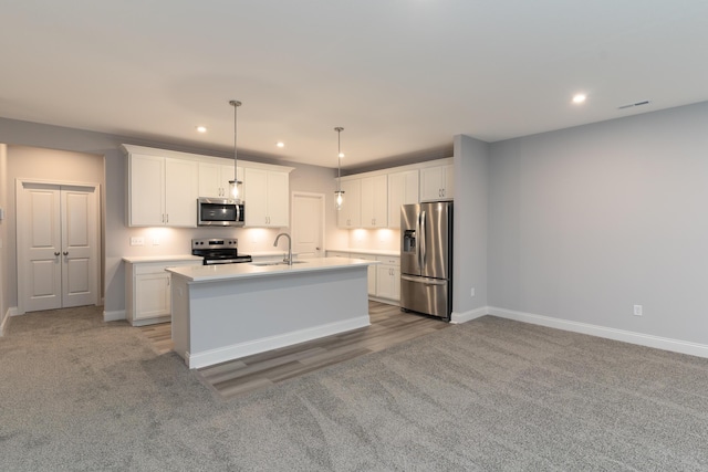 kitchen featuring white cabinetry, stainless steel appliances, decorative light fixtures, and a kitchen island with sink