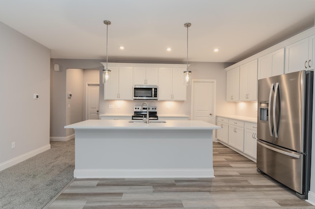 kitchen featuring white cabinetry, stainless steel appliances, hanging light fixtures, and a center island with sink