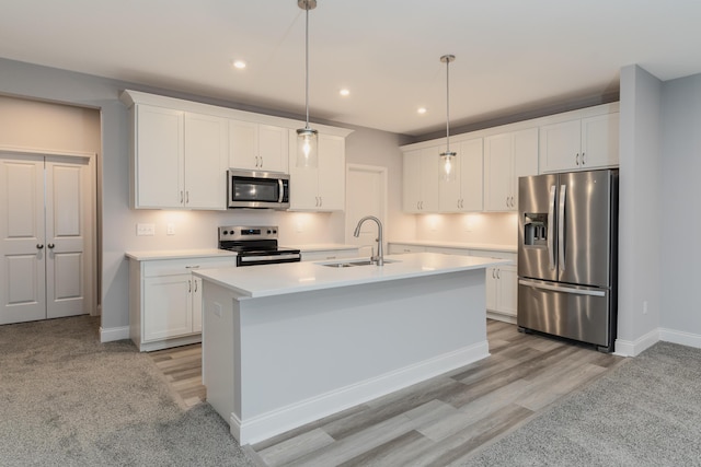 kitchen featuring sink, appliances with stainless steel finishes, white cabinetry, a kitchen island with sink, and hanging light fixtures