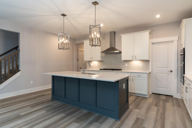 kitchen featuring sink, decorative light fixtures, white cabinetry, and wall chimney range hood