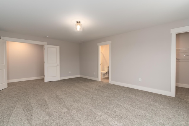 unfurnished bedroom with carpet, a walk in closet, connected bathroom, and a closet