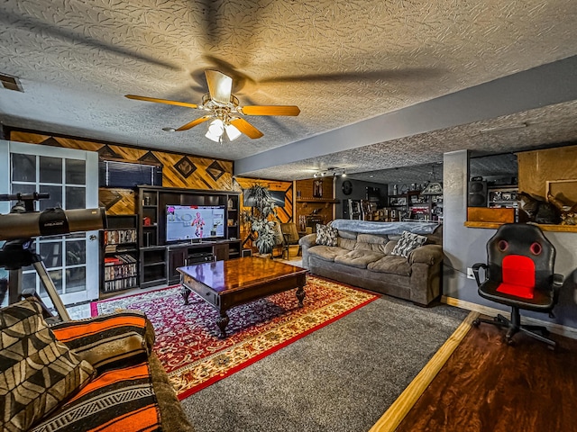 living room featuring ceiling fan, a textured ceiling, and wood walls