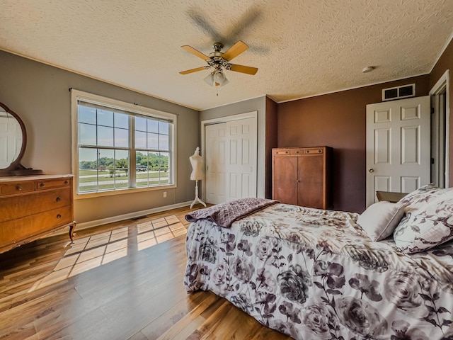 bedroom with light hardwood / wood-style flooring, a textured ceiling, ceiling fan, and a closet