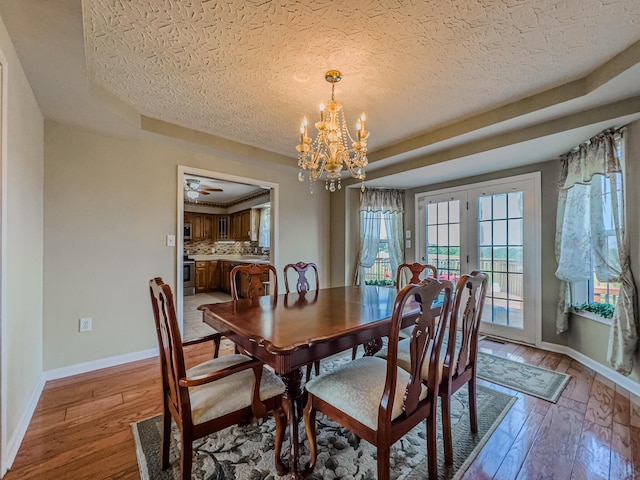 dining room featuring french doors, a raised ceiling, light hardwood / wood-style floors, and a textured ceiling