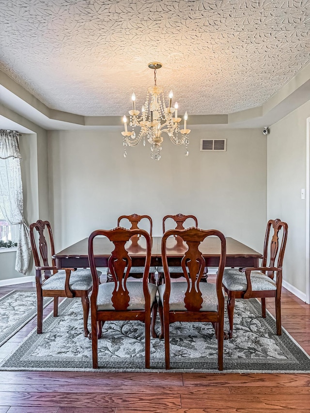 dining space with hardwood / wood-style floors, a textured ceiling, and a chandelier