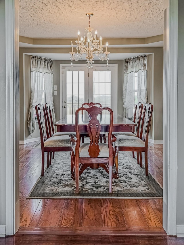 dining area featuring hardwood / wood-style flooring, a chandelier, a textured ceiling, and french doors