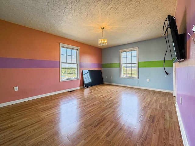 unfurnished living room with plenty of natural light, a chandelier, hardwood / wood-style floors, and a textured ceiling