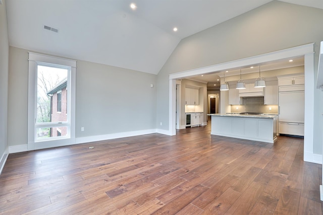 unfurnished living room featuring dark hardwood / wood-style flooring, beverage cooler, and high vaulted ceiling