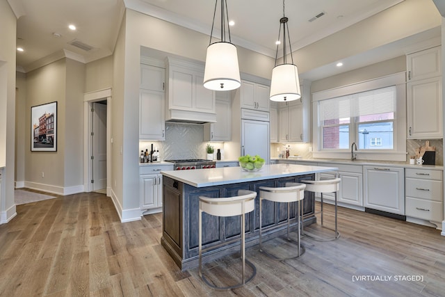 kitchen featuring white cabinets, paneled built in fridge, a kitchen breakfast bar, hanging light fixtures, and a kitchen island