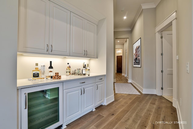 bar with beverage cooler, crown molding, white cabinetry, and light hardwood / wood-style flooring