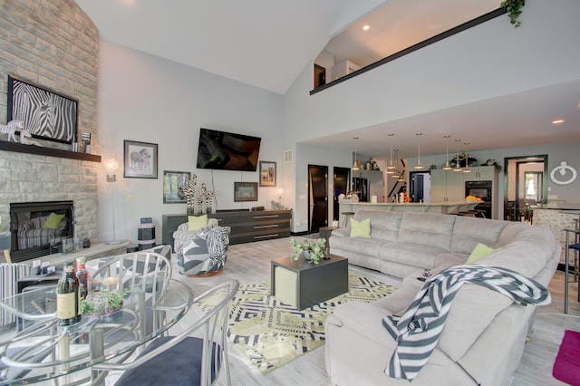 living room with a stone fireplace, high vaulted ceiling, and light hardwood / wood-style floors