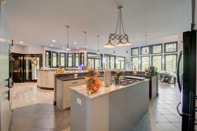 kitchen with black fridge, dark stone countertops, decorative light fixtures, a center island, and white cabinets