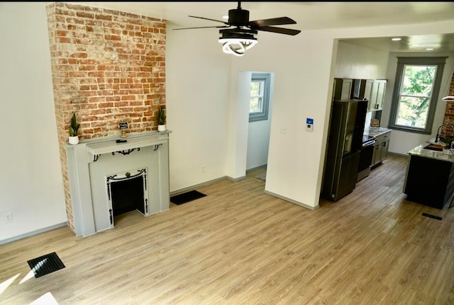 unfurnished living room with sink, ceiling fan, brick wall, and light hardwood / wood-style flooring