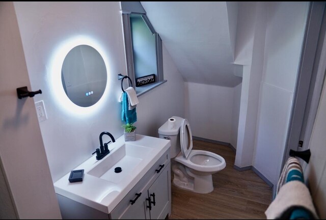 bathroom featuring hardwood / wood-style flooring, vaulted ceiling, toilet, and vanity