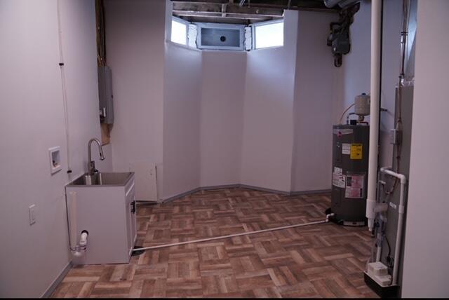 clothes washing area with parquet floors, sink, and water heater